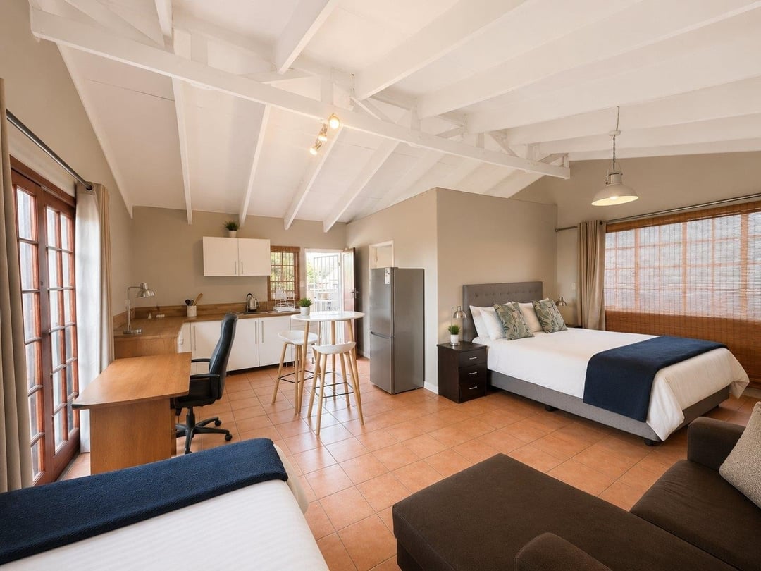 Upstairs studio under a white-beamed pitched ceiling, with a kitchenette, desk and double bed