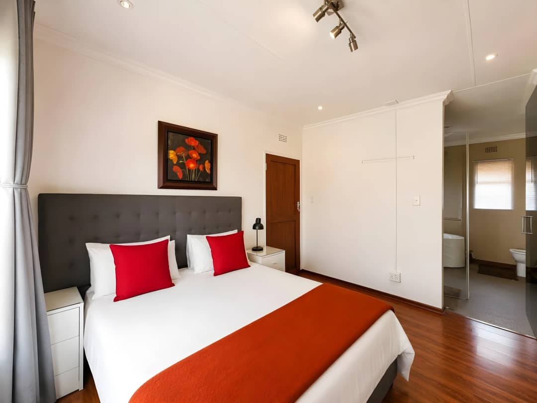 Main bedroom with a charcoal headboard and red accents, opening into the en-suite bathroom